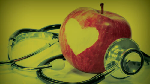 An apple with a heart cut into it sitting on a stethoscope