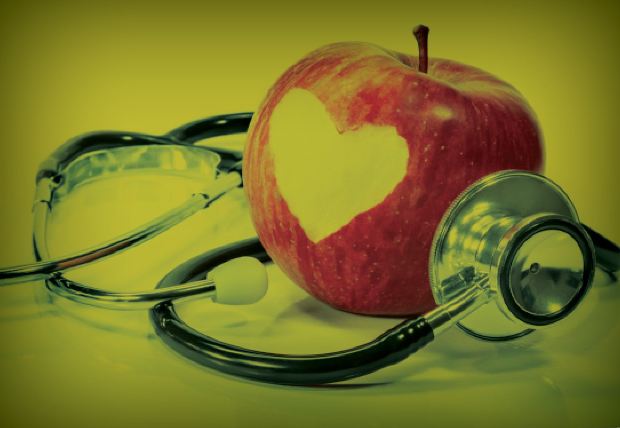 An apple with a heart cut into it sitting on a stethoscope