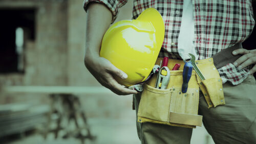 A construction worker holding a hard hat in one hand by his leg