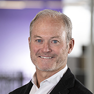 John Hurley - a man in a suit without a tie is smiling for a professional headshop photo
