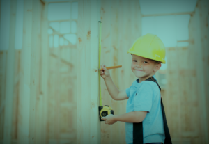 A boy in a hard hat measuring wood