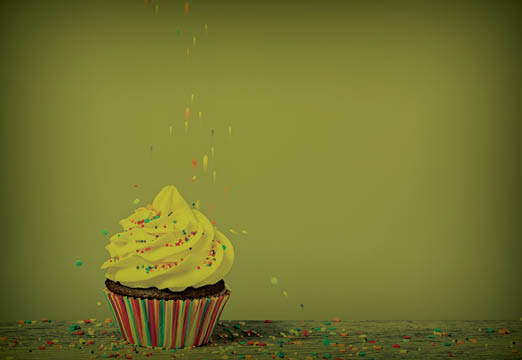 A Cupcake with sprinkles falling on it.