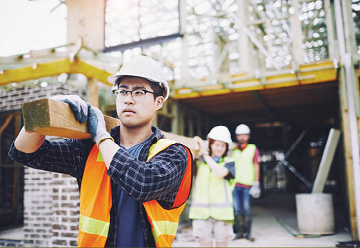 A construction worker holding some beams of wood while working.