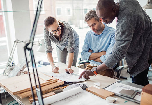 three employees pointing at paperwork on a desk.