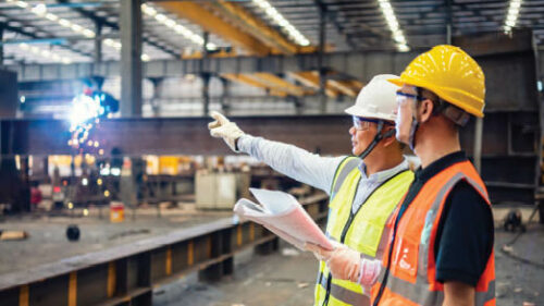 Two workers wearing safety vests in a warehouse setting