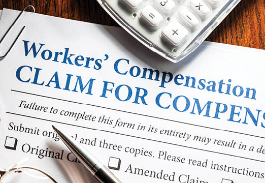 A workers compensation claim form with a pen and calculator on a desk