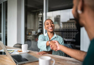 Two people shaking hands over a conference table.