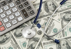 A calculator and a stethoscope sitting on top of a lot of dollar bills.