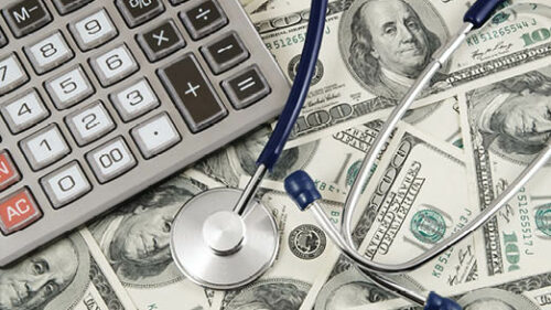 A calculator and a stethoscope sitting on top of a lot of dollar bills.