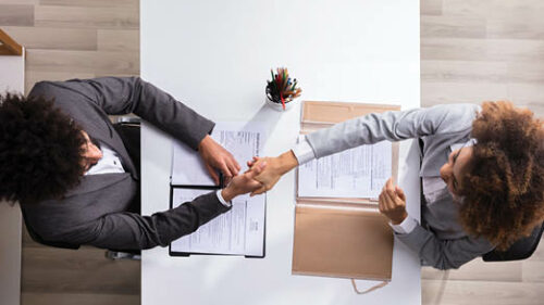 Two business women shaking hands over a contract on a table