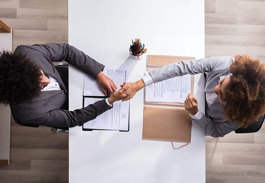 Two business women shaking hands over a contract on a table