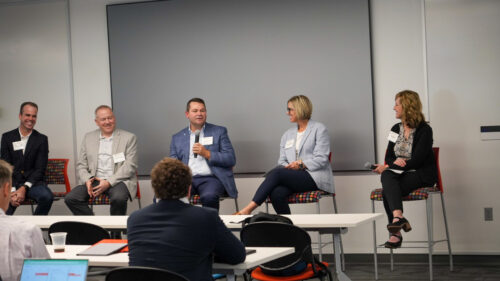 Business professionals sitting in chairs as a panel in front of an audience.