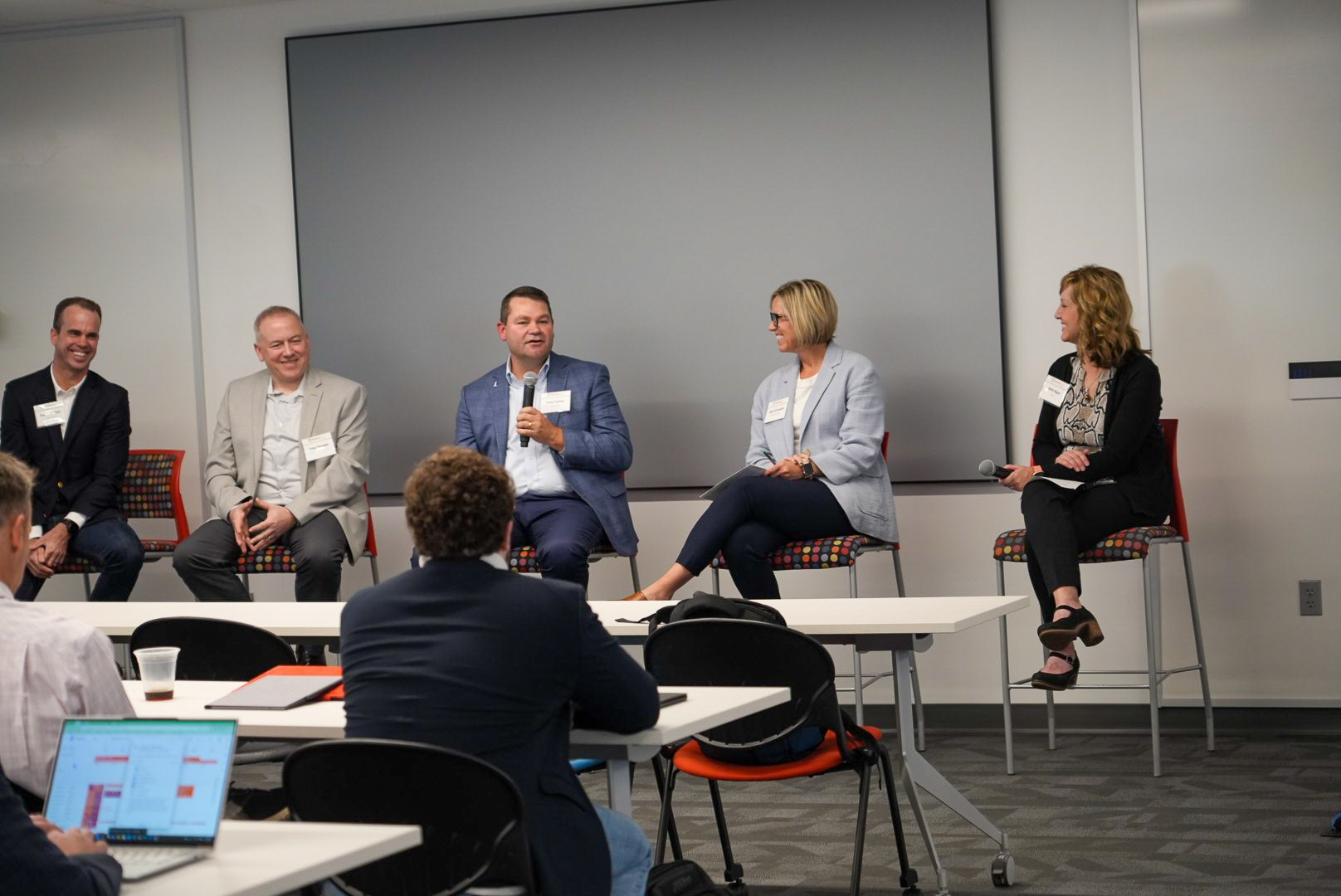 Business professionals sitting in chairs as a panel in front of an audience.
