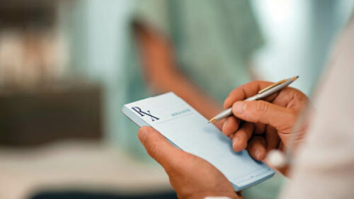 The hands of a doctor writing on the prescription pad.