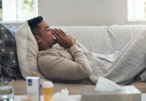 A man laying on a couch while blowing his nose with a tissue.