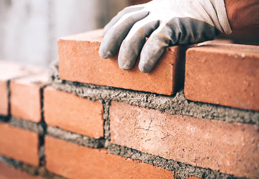 A gloved hand laying brick and building a wall