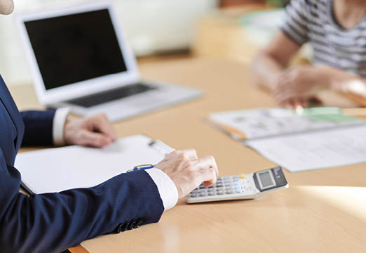 two business professionals sitting at a table with papers, a laptop and calculators scattered on top.