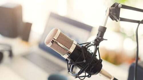 A podcast mic hanging in front of a laptop on a desk.