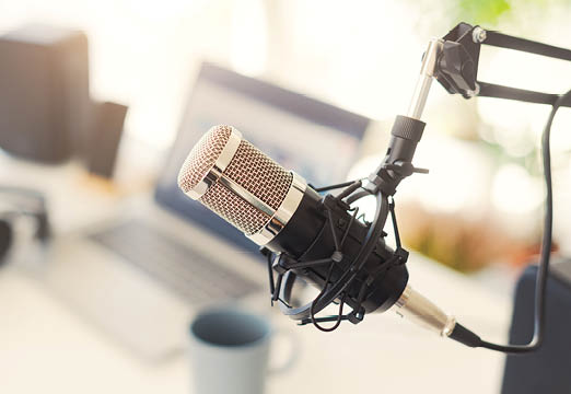 A podcast mic hanging in front of a laptop on a desk.