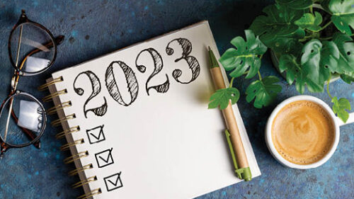 A coffee cup, glasses and a notebook with 2023 written on it on a desk