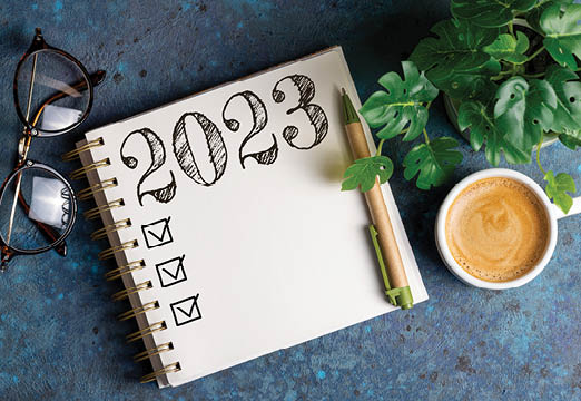 A coffee cup, glasses and a notebook with 2023 written on it on a desk