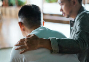 A man's slumped back with another man comforting him with his arm around his shoulder.