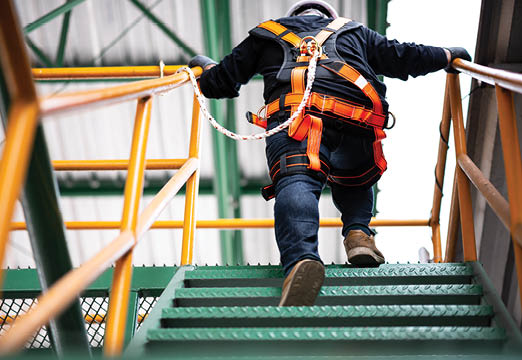A worker climbing construction stairs wearing a safety harness