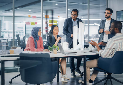 A multicultural group of design professionals discussing a model building in a conference room