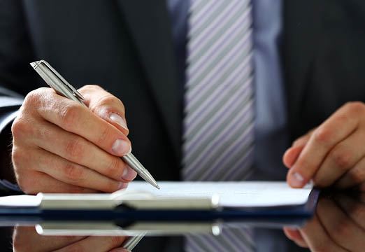 A business professional holding a pen and signing insurance paperwork.