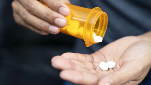 A hand pouring out prescription pills.