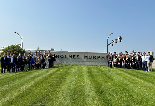 A group photo of the class of 2023 Holmes Murphy interns in front of the Holmes Murphy sign on a green lawn.