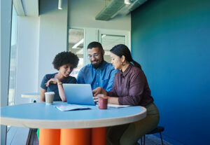 Three happy employees sitting around a laptop.