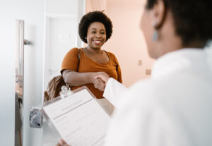 A Black woman shaking hands with a doctor who is a woman too.