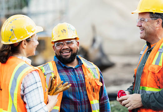 Three construction workers in safety gear talking on a job site.