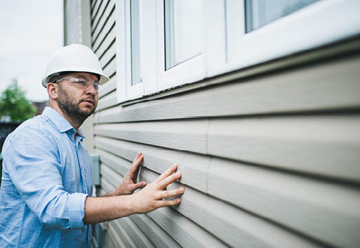 A man in a hardhat inspecting siding of a house.