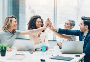 A group of diverse employees around a conference table high fiving.