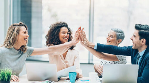 A group of diverse employees around a conference table high fiving.