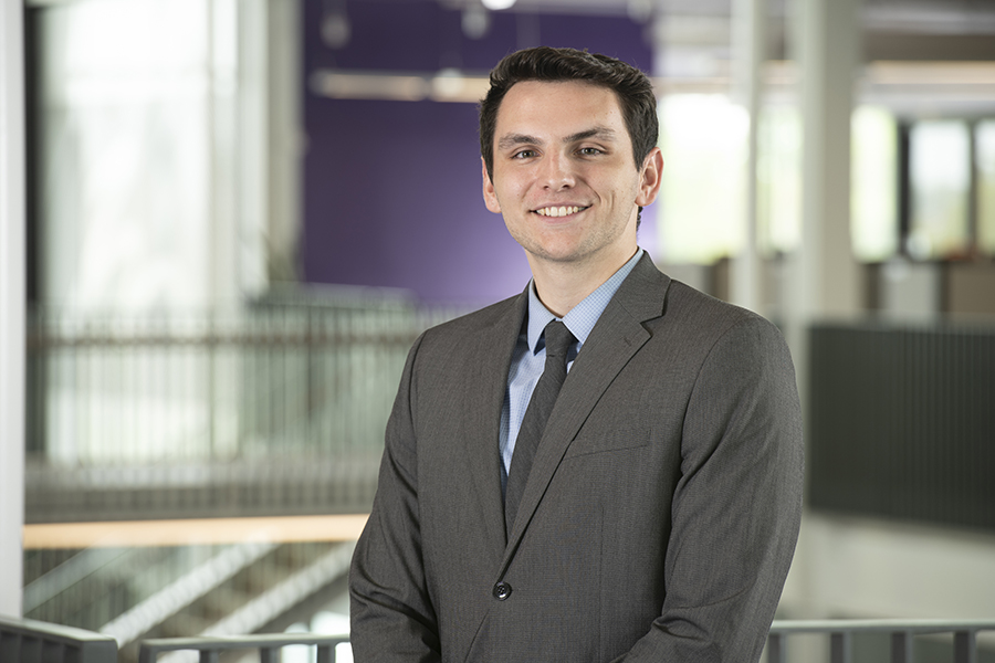 A young man in a grey suit smiling for a professional photo.