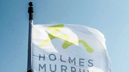 Holmes Murphy logo on a flag with blue sky