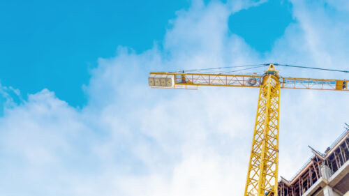 tall yellow crane next to a metal and concrete building under construction