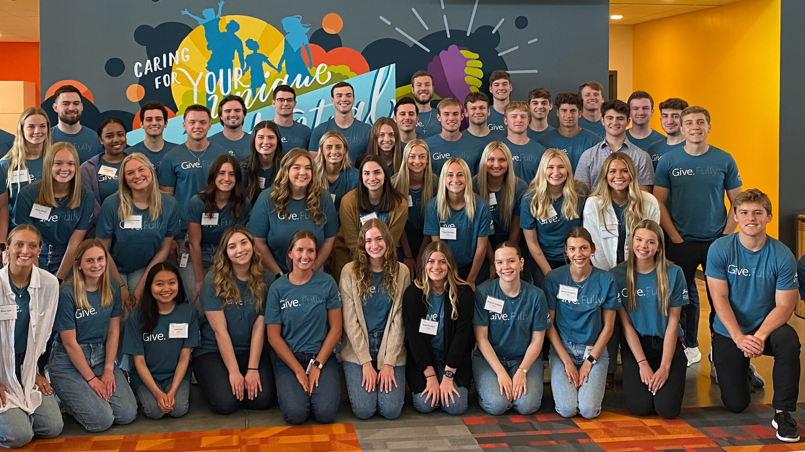 The summer 2023 interns standing as a large group in front of a mural in the office.