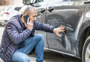 A man examining a car that has been hit.