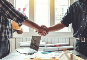 Two construction professionals shaking hands over a desk.
