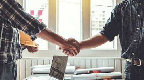 Two construction professionals shaking hands over a desk.