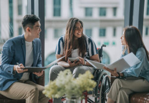 Three employees chatting, one uses a wheelchair.