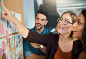 Three employees collaborating around a cork board planning together.
