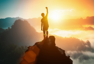 A person pumping their fist on the top of the mountain