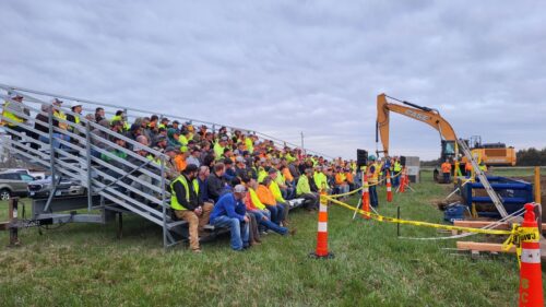 A group of construction workers sitting on bleachers, listening to OSHA presentation.