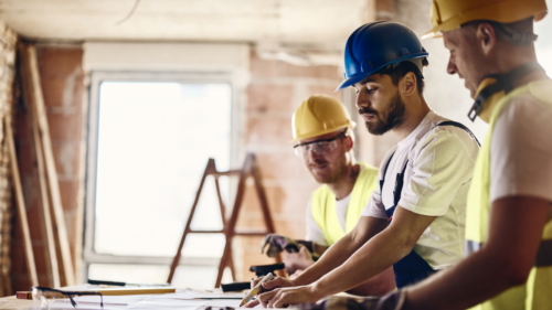 Three construction workers evaluate plans while working