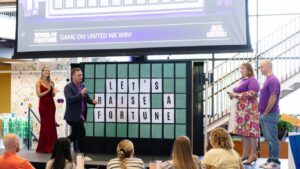 Holmes Murphy employees reveal a Wheel of Fortune-inspired board that says Let's Raise A Fortune in honor of United Way Week